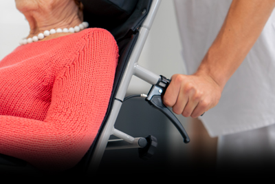 caregiver assisting elderly woman in wheelchair with comfortable knit sweater and pearls, mobility aid support